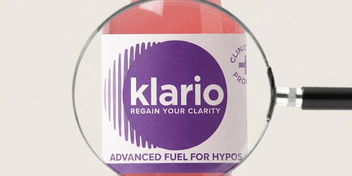 A magnifying glass held over a bottle of Klario, enlarging the label's logo and 'Advanced fuel for hypos' wording